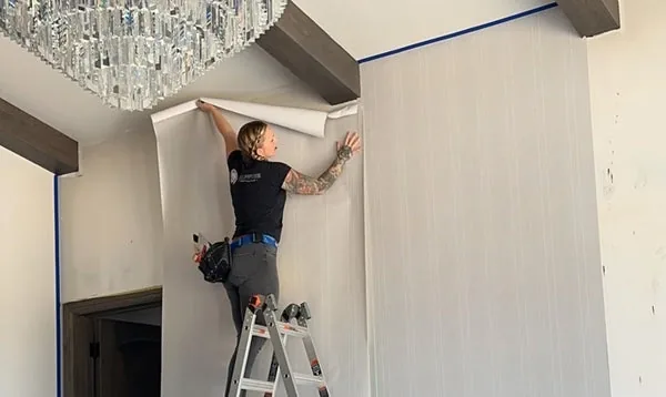 Installer working from a ladder to hang wallpaper near a ceiling line