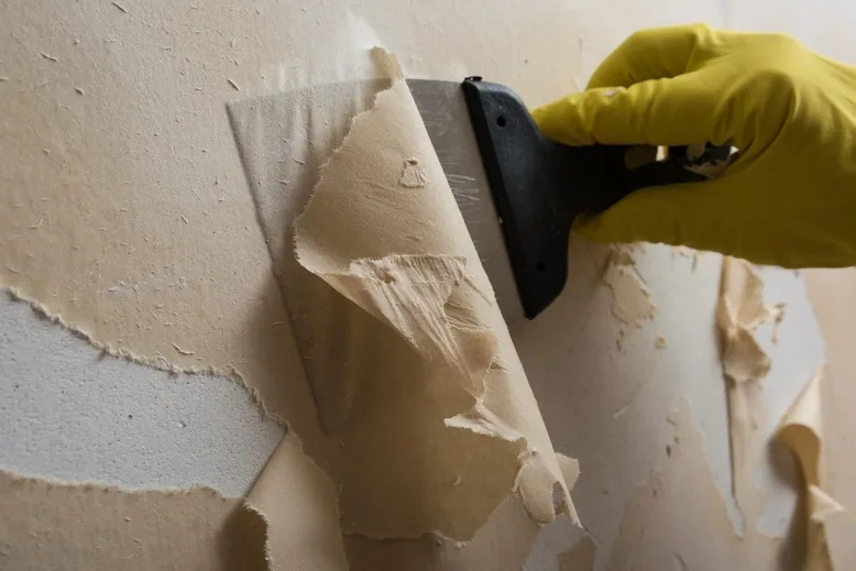 Professional wallpaper removal — technician scraping old wallpaper cleanly from drywall